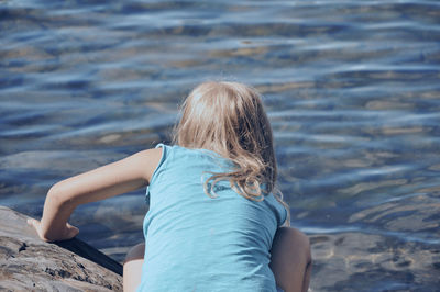 Rear view of woman sitting on rock by sea