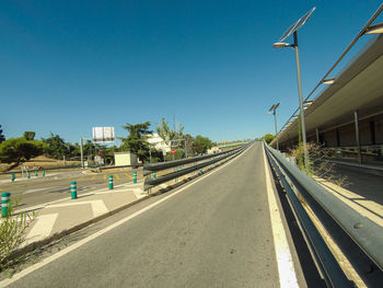 Empty road by buildings against clear blue sky