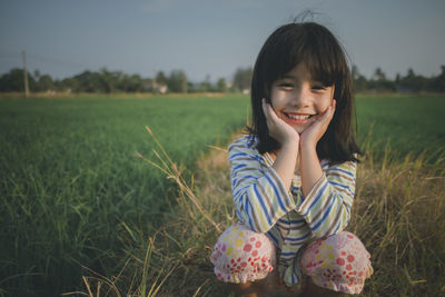 Portrait of cute girl crouching on grassy field against sky