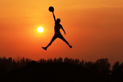 Midsection of silhouette man catching ball in mid-air against orange sky