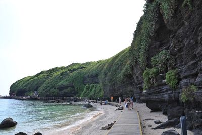 People on rocks by sea against clear sky