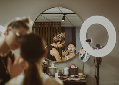 A young makeup artist applies protective cream to a girl s face.