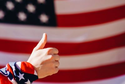 Cropped hand gesturing thumbs up sign against american flag