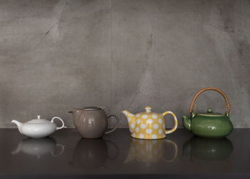 Close-up of teapots on table against wall