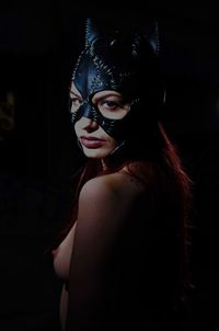 Portrait of shirtless woman in eye mask standing by black background