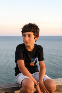 Boy sitting in sea against sky