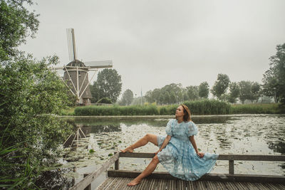 Woman sitting by lake against sky