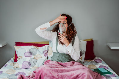 Woman wearing oxygen mask while sitting against wall in hospital