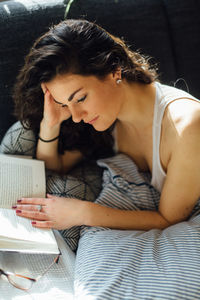 High angle view of woman reading book while lying on bed at home