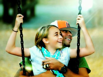 Father embracing cute daughter while sitting on swing at park