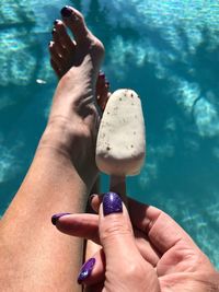 Low section of woman holding ice cream candy over swimming pool