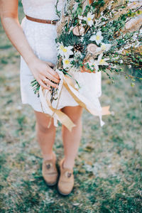 Low section of bride holding bunch of flowers at field