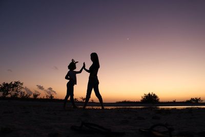 Silhouette woman and girl giving high-five against sky during sunset