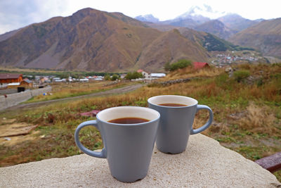 Two cups of on the stone table with blurry countryside view in the backdrop