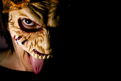 Close-up portrait of woman wearing mask while sticking out tongue against black background