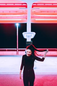 Young woman holding hair standing on illuminated city street at night