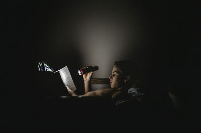 Boy holding flash light while reading book at home