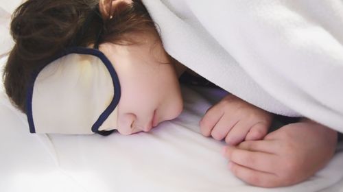 Girl wearing sleep mask while sleeping on bed
