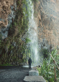 Rear view of man looking at waterfall while he is standing directly below the waterfall. 