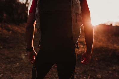 Rear view of man with backpack standing on field during sunset