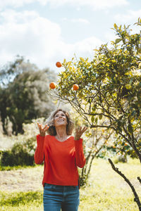 Happy woman juggling oranges standing by tree in garden