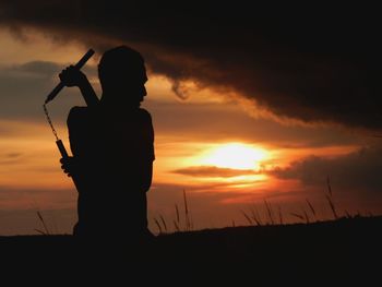 Silhouette man practicing martial arts with nunchaku during sunset