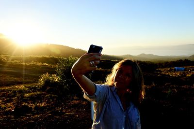 Woman taking selfie through mobile phone while standing on field