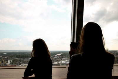 Rear view of woman standing by window against sky