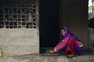 Portrait of smiling woman sitting entrance og village kitchen grinding spice for food