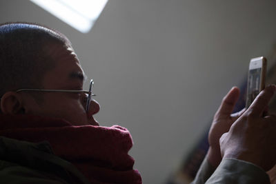 Side view of man using mobile phone while sitting against wall