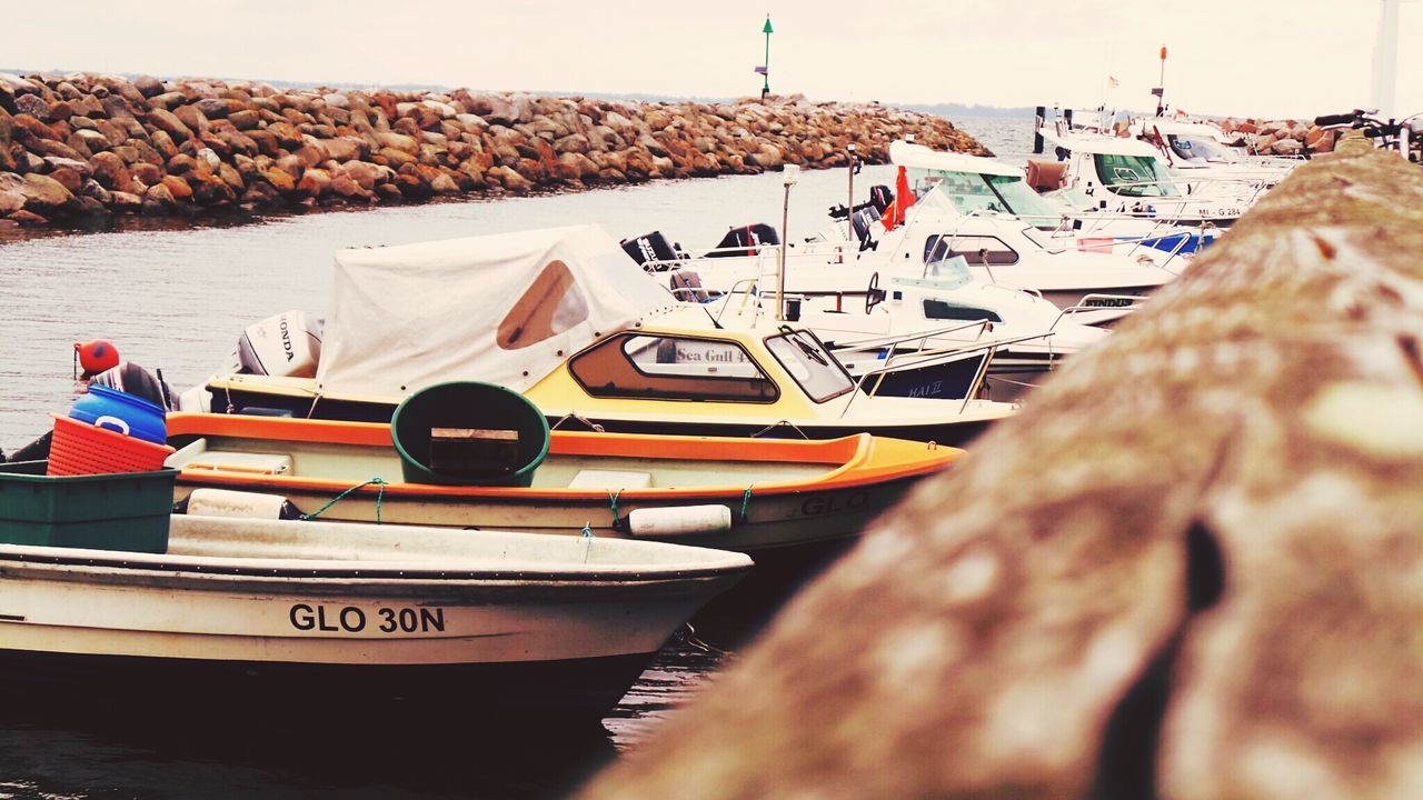 sea, multi colored, water, nautical vessel, day, beach, boat, no people, moored, flag, text, outdoors, sky, close-up, transportation, focus on foreground, wood - material, in a row, sunlight, large group of objects