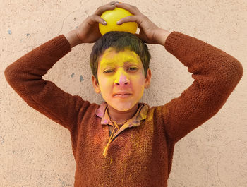 Portrait of a boy covered with holi color and holding ballon with standing against wall