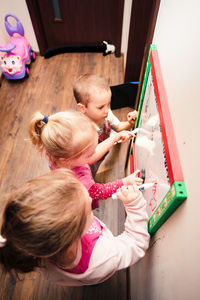 High angle view of siblings writing on whiteboard at home