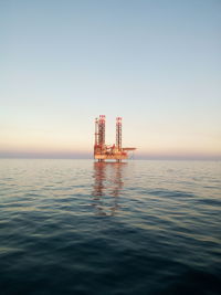 Offshore platform in sea against clear sky during sunset
