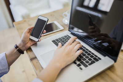 Close-up of woman at wooden desk with cell phone and laptop