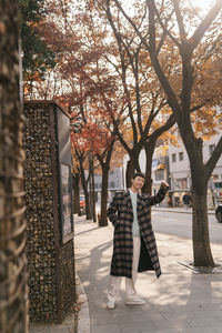 Woman walking on footpath by street in city during autumn