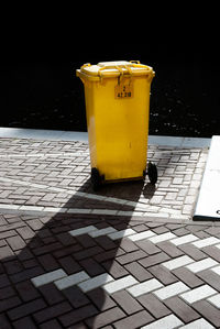 Yellow garbage can on footpath during sunny day