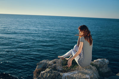 Woman sitting on rock by sea against sky