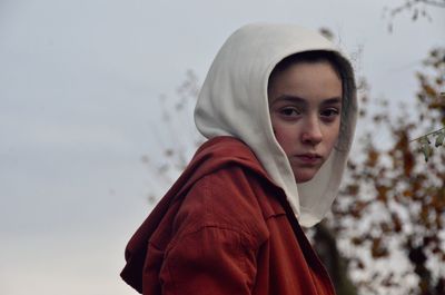 Close-up portrait of young woman wearing hooded shirt against sky