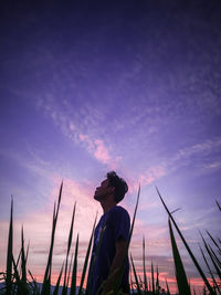 Low angle view of man standing amidst plants against sky during sunset