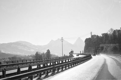 Road by snow covered mountain against clear sky