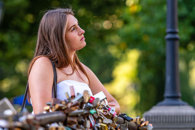 Young woman looking away while siting by padlocks outdoors