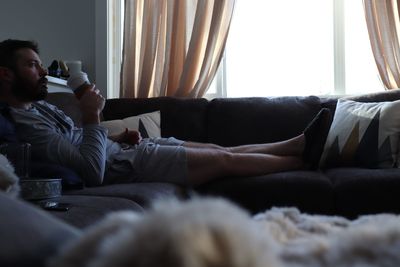 Young man drinking coffee while relaxing on sofa at home