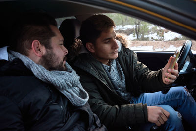 Two young men look at a phone inside a car. concept of route finding