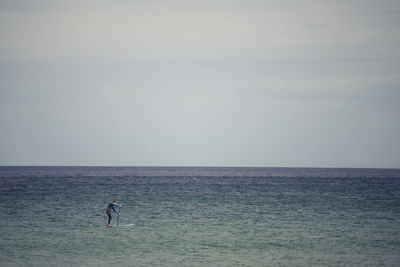 Distant view of man surfboarding in sea against sky