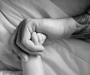 Close-up of cropped hand holding child leg on bed at home