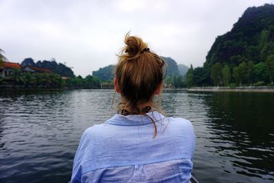 Rear view of woman by lake against sky