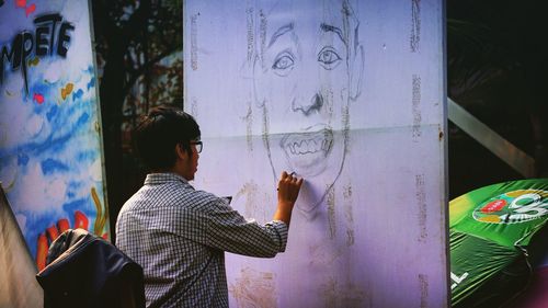 Rear view of young man drawing on board while standing outdoors