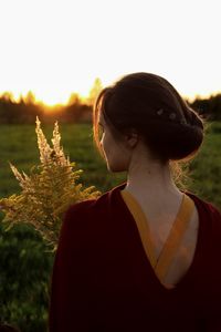Portrait of young woman standing on field against sky during sunset