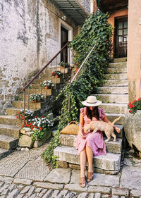 Full length portrait of a beautiful young woman in old town, lifestyle, pink dress, petting a cat.